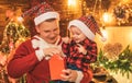 Smiling father and his son in Santa& x27;s hat open a Christmas gift present box. New Year tree and fire place at Royalty Free Stock Photo