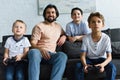 smiling father looking at little sons sitting on sofa and playing video games together Royalty Free Stock Photo