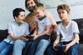 smiling father looking at little sons sitting on sofa and playing video games together Royalty Free Stock Photo