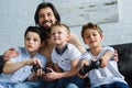 smiling father looking at little sons sitting on sofa and playing video games together Royalty Free Stock Photo