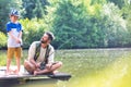 Smiling father looking at son standing on pier while fishing in lake Royalty Free Stock Photo