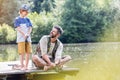 Smiling father looking at son standing on pier while fishing in lake Royalty Free Stock Photo