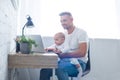 smiling father sitting on chair, holding baby and using laptop Royalty Free Stock Photo