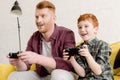 smiling father and son sitting on sofa and playing with joysticks Royalty Free Stock Photo