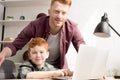 smiling father and son using laptop together and looking at camera Royalty Free Stock Photo