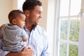 Smiling Father Standing By Window With Baby Son At Home