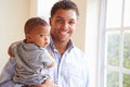 Smiling Father Standing By Window With Baby Son At Home Royalty Free Stock Photo