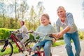 Smiling father with two daughters during outdoor walk. He teaching younger girl to ride a bicycle. They enjoy togetherness in the