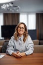 Smiling female employee office worker in glasses, sitting at desk on workplace, looking at camera. Job interview