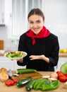 Smiling female chef in black uniform offering plate of vegetable salad Royalty Free Stock Photo