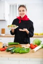 Smiling female chef in black uniform offering plate of vegetable salad