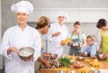 Smiling female chef sharing professional secrets during cooking masterclass for children Royalty Free Stock Photo