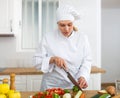 Smiling female chef in white uniform preparing vegetable salad in private kitchen