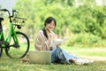 Smiling female college student doing homework and using laptop on campus lawn during sunny day Royalty Free Stock Photo