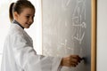 smiling female college student writing on blackboard during chemistry lesson, schoolgirl in white coat writing formulas Royalty Free Stock Photo
