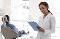 Smiling female dentist filling medical form in cabinet