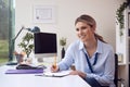 Smiling Female Doctor Or GP Sitting At Desk In Office Writing Notes On Clipboard Royalty Free Stock Photo