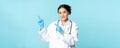 Smiling female doctor, physican in medical uniform and sterile gloves, pointing fingers left at promo, clinic logo