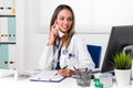 Smiling female Doctor sat at desk with telephone to ear Royalty Free Stock Photo