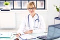 Smiling female doctor sitting at desk and doing some paperwork Royalty Free Stock Photo