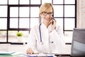 Smiling female doctor using phone and talking with her patient while sitting in doctor`s office Royalty Free Stock Photo