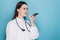 Smiling female doctor wearing white medical uniform and stethoscope holding phone speak activate virtual digital voice assistant Royalty Free Stock Photo