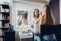 Smiling female esthetician applying makeup using brush to the female model in stylish beauty studio