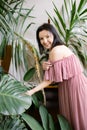 Smiling female florist shows large monstera leaf in her greenhouse. Hobby. Home greenhouse. Top dressing with plants.