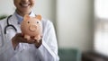 Smiling female GP doctor holding piggy bank on hands Royalty Free Stock Photo