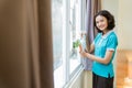 smiling female housekeeper in turquoise uniform wiping windows