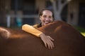 Smiling female jockey leaning on horse at barn Royalty Free Stock Photo