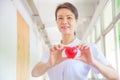Smiling female nurse holding red smile heart in her hands. Red heart Shape representing high quality service mind to patient.
