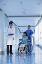 Smiling female nurse pushing and assisting patient in a wheelchair in the hospital, talking to doctor Royalty Free Stock Photo