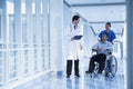 Smiling female nurse pushing and assisting patient in a wheelchair in the hospital, talking to doctor Royalty Free Stock Photo