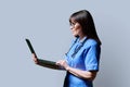 Female nurse using laptop, profile view on gray studio background Royalty Free Stock Photo