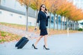 Smiling female passenger proceeding to exit gate pulling suitcase through airport concourse Royalty Free Stock Photo