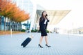 Smiling female passenger proceeding to exit gate pulling suitcase through airport concourse