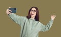 Female student blogger in glasses and casual clothes takes selfie or records story for Instagram.