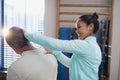 Smiling female therapist examining neck of senior male patient