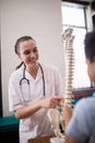 Smiling female therapist explaining boy while pointing at artificial spine against wall Royalty Free Stock Photo