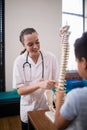 Smiling female therapist explaining boy while pointing at artificial spine Royalty Free Stock Photo