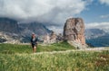 Smiling female trekker walking with backpack and trekking poles by green mountain hill with picturesque Dolomite Alps Cinque Torri Royalty Free Stock Photo