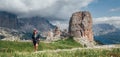 Smiling female trekker walking with backpack and trekking poles by green mountain hill with picturesque Dolomite Alps Cinque Torri Royalty Free Stock Photo