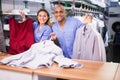 Smiling female worker of modern laundry standing with her colleague at reception counter, showing clean clothing and