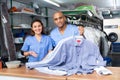 Smiling female worker of modern laundry standing with her colleague at reception counter, showing clean clothing and