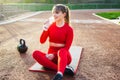 Smiling fitness woman drinking water from a reusable glass bottle while taking rest sitting on a mat in the stadium Royalty Free Stock Photo