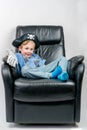 Smiling five year old boy dressed up in a pirate and police officer costume sit and laze in an black leather armchair.