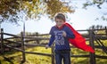 Smiling five year old boy running with red cape outside