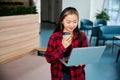 Smiling and focused asian female IT employee with coffee watching laptop in hall