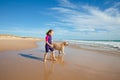 Smiling little girl walking with a dog on the shore of beach